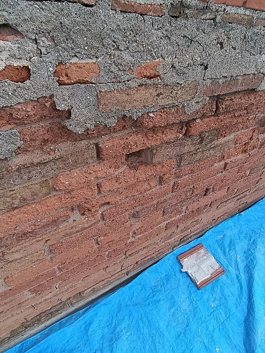 Antes: base de la medianera de ladrillo, con el mortero suelto y la lona de protección
