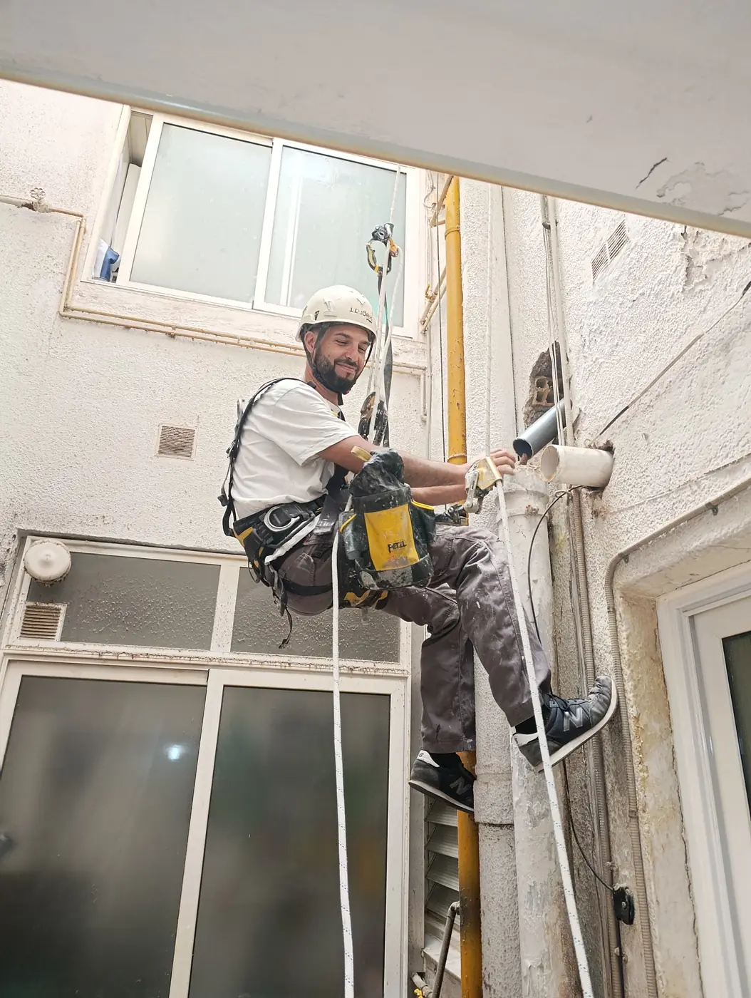 Técnico colgado con cuerdas sustituyendo un bajante en un patio de luces