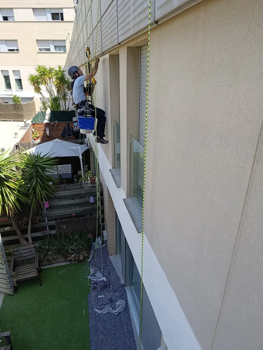 Técnico colgado con cuerdas trabajando en la fachada de un edificio de viviendas