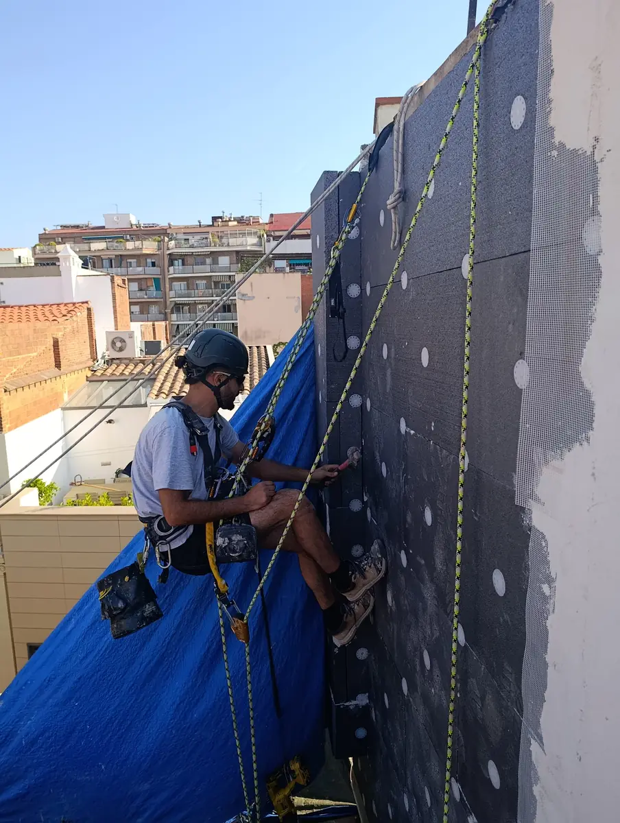 Técnico colgado con cuerdas trabajando en una medianera