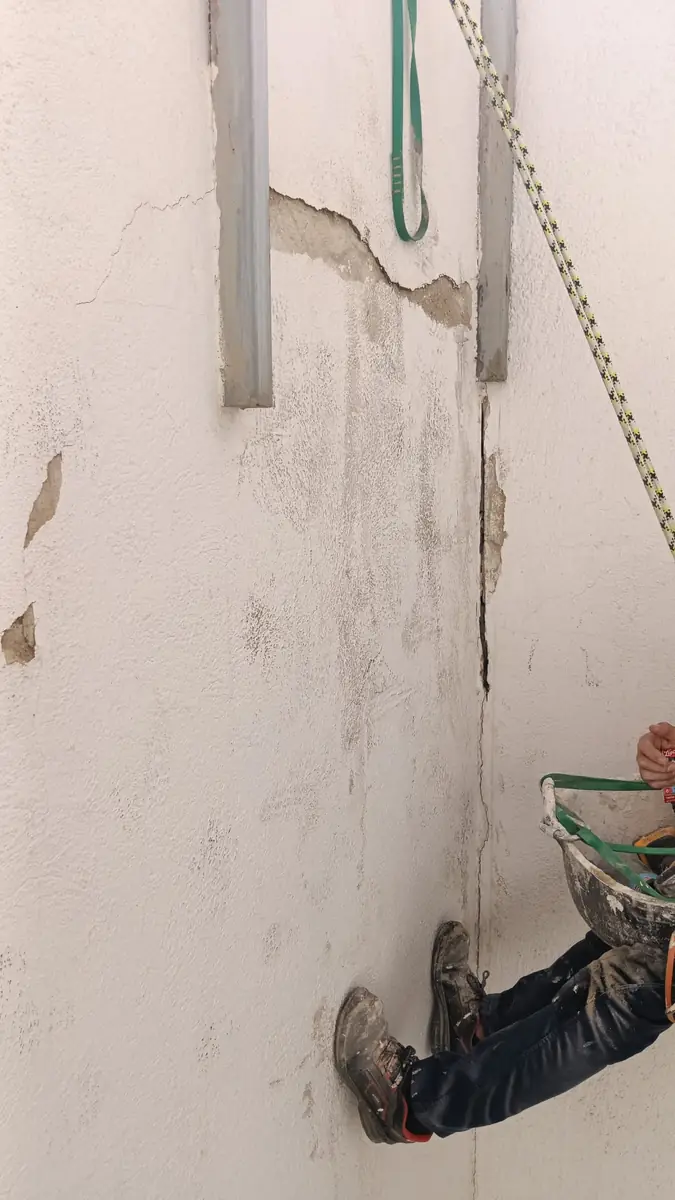 Técnico suspendido con cuerdas junto a la pared de un patio de luces