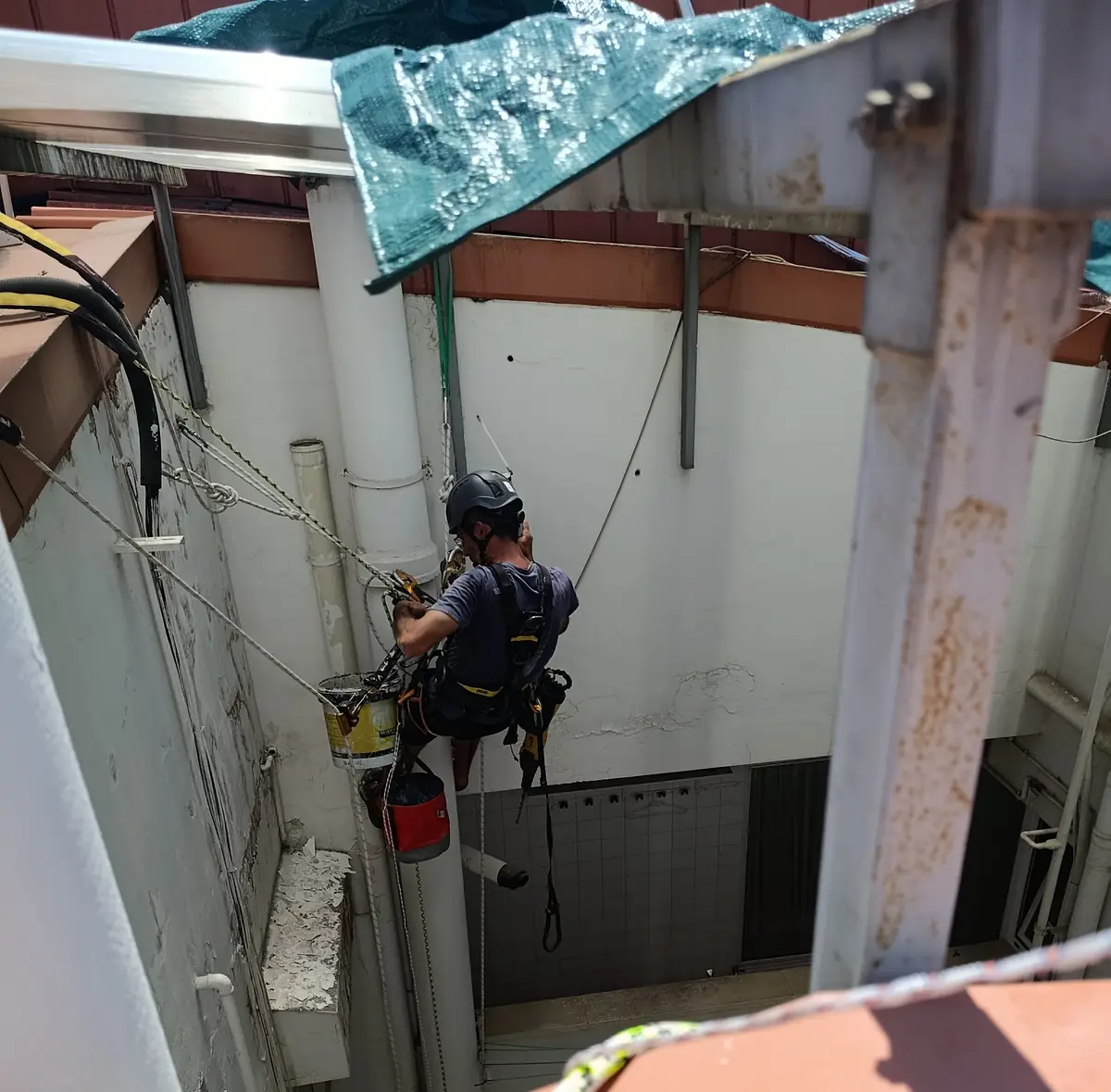 Técnico colgado trabajando en un patio de luces, visto desde la azotea