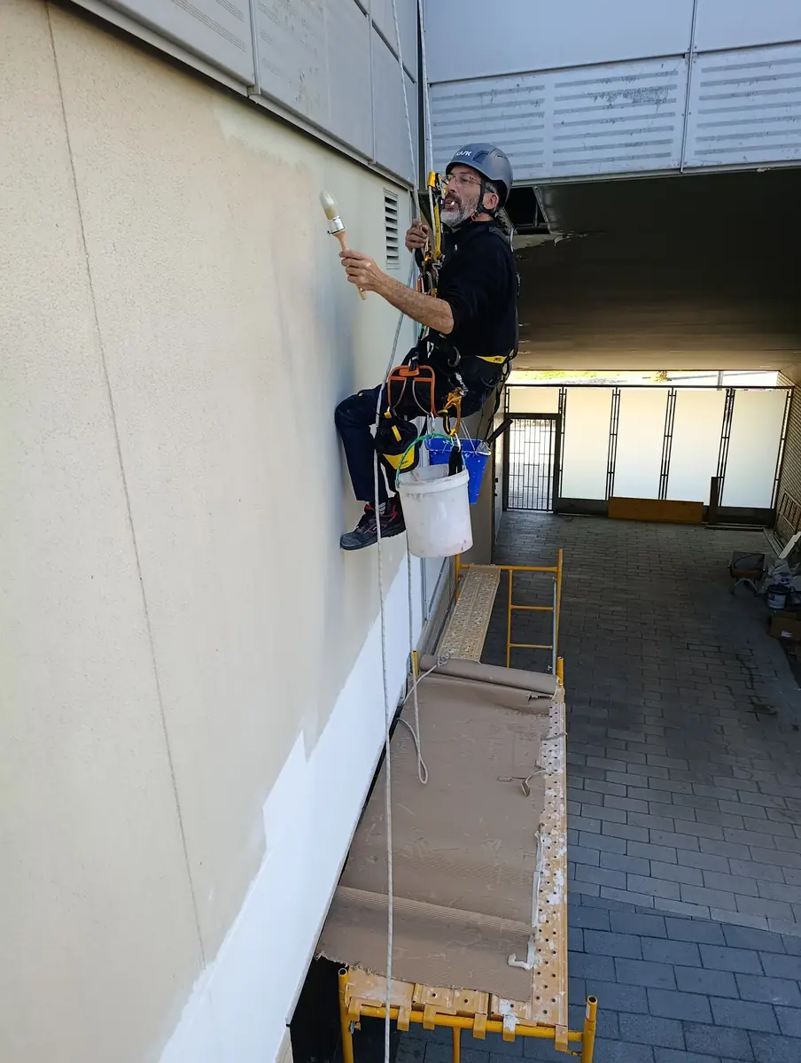 Técnico colgado pintando una fachada con trabajos verticales