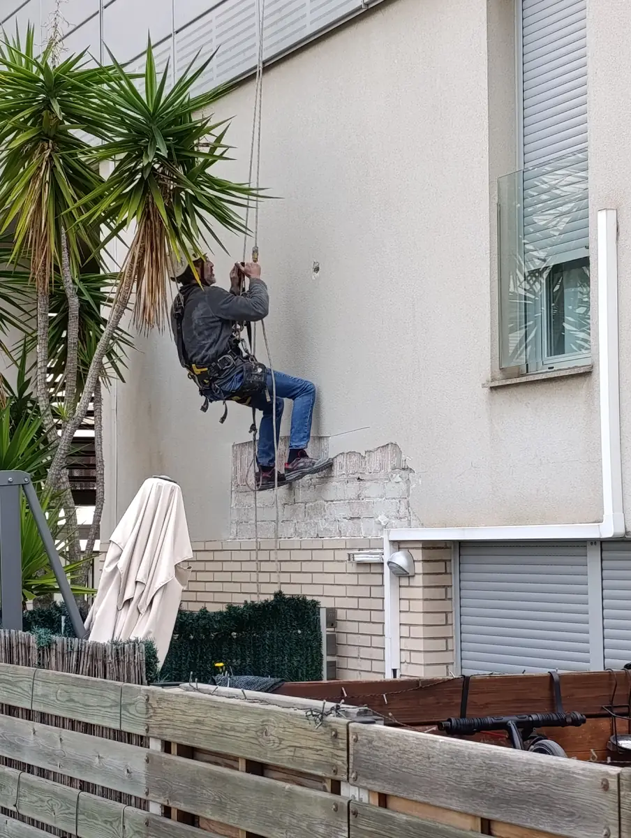 Técnico colgado reparando el revestimiento de una fachada